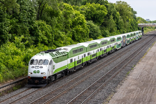 Toronto Canada, June 10 2024; A GO Transit commuter train against a green forest backdrop with a bridge in the distance