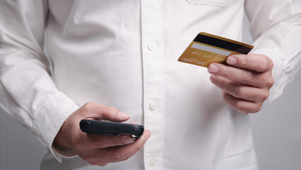 A man is holding a credit card and a cell phone. He is using the smartphone to pay for online shopping or e-commerce. Internet online payment concept.