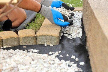 Laying an anti-weed mat in the garden together with paving stones and decorative pebbles