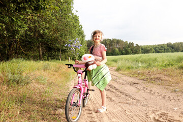Fototapeta premium A ten-year-old girl with a bouquet of flowers on a bicycle walks along a forest road
