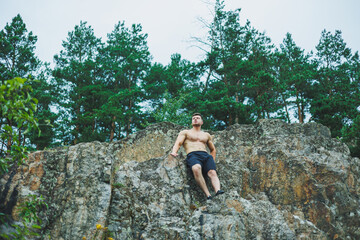 Naklejka premium A young man with abs cubes on the background of the forest. Athletic pumped-up man on a rock background.