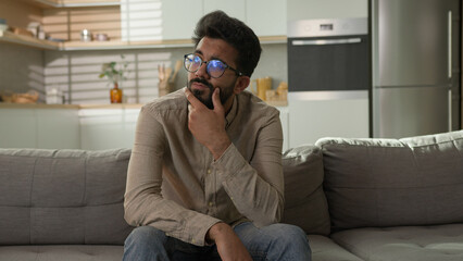 Pensive thoughtful Indian Arabian ethnic man puzzled guy at home apartment kitchen think difficult...