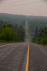 A country road leading down a large hill to a rural smokey Forested Area