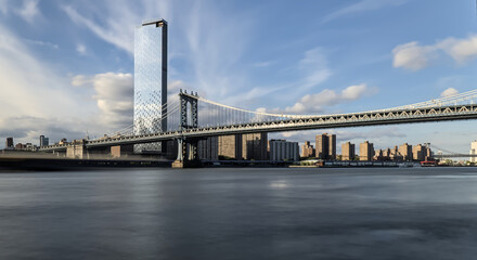 view of manhattan bridge over hudson river with blue sky (long exposure downtown brooklyn skyline view) travel tourism destination new york city skyscraper