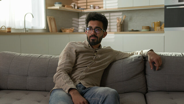 Bored unhappy tired Arabian Indian man millennial ethnic guy exhausted male homeowner relax on sofa watch television in kitchen lazy weekend watching TV channel boring rest at home couch after work