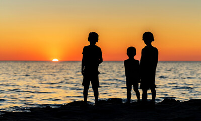 some children watching a sunset at the sea