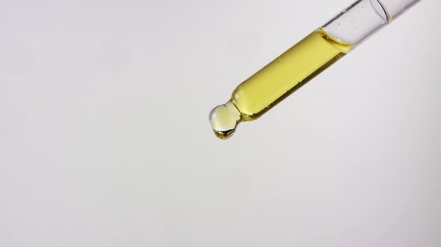 Close up of oil dropping from a dropper on isolated white background