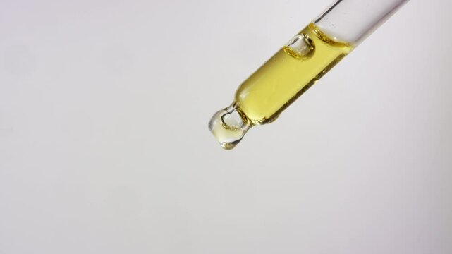 Close up of oil dropping from a dropper on isolated white background