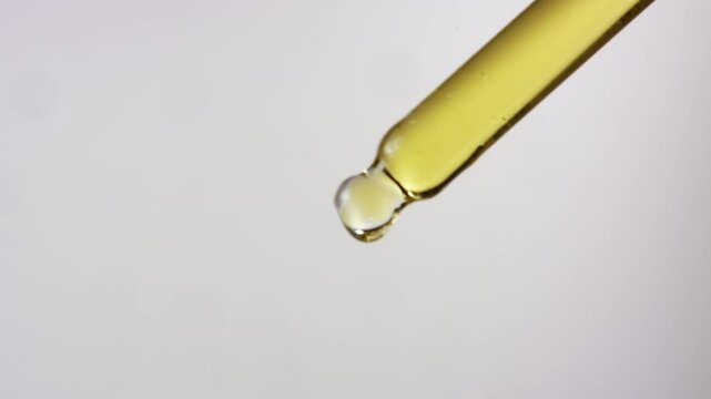 Close up of oil dropping from a dropper on isolated white background