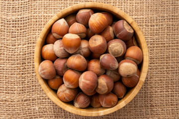 Overhead view of a wooden bowl full of shelled hazelnuts on a piece of burla