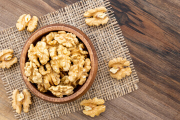 Overhead view of a bowl full of walnut kernels on a wooden surface. A piece of burlap and a few walnut kernels lying around