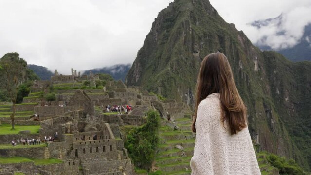 Girl in White Poncho Overlooking Historic Machu Picchu. A girl wearing a white poncho, gazing at the historic site of Machu Picchu, exploring a new culture and enjoying her vacation