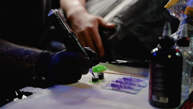 A professional tattoo artist, wearing black gloves, prepares for a session with a tattoo machine