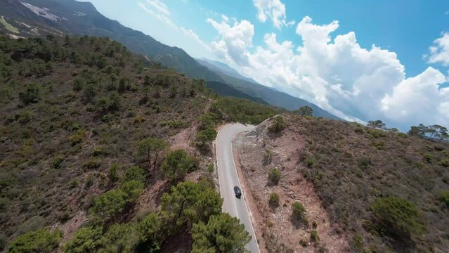 Aerial FPV drone captures a beautiful mountain road scene with a car under a cloudy sky