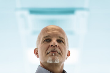 Thoughtful old man gazes upward, blue background blurred