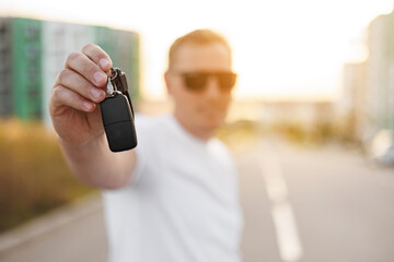 Adult male driver holds new car key with fob outdoors, remote control car alarm systems. Selective focus. Man in sunglasses rents, sales or buys vehicle. Concept of financial possibility and lifestyle
