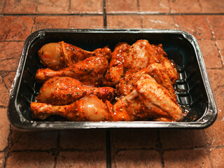 A tray of chicken wings and drumsticks is sitting on a counter. The product is covered in a sauce and are ready to be cooked. Asian style marinated poultry. Barbeque style food.