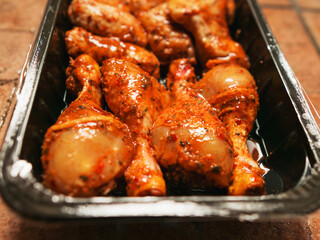 A tray of chicken wings and drumsticks is sitting on a counter. The product is covered in a sauce and are ready to be cooked. Asian style marinated poultry. Barbeque style food.
