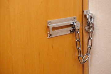 A brown color wooden door with a strong metal chain and a lock on it. The lock is silver and the chain is silver as well. Safety and security concept.