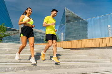 A fit couple energetically runs down stairs in an urban setting, enjoying their active lifestyle...