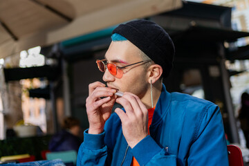 Young man eating hamburger in street cafe with stylish look