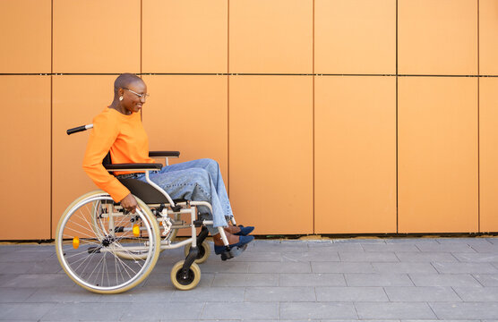 Smiling woman in wheelchair by orange wall