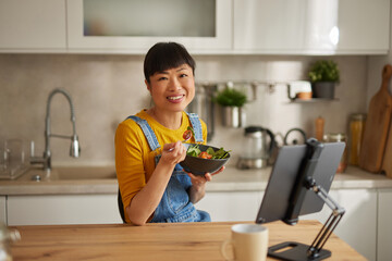 An Asian woman eating healthy salad in the kitchen