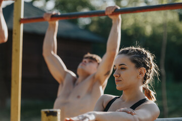 Two young adults working out on pull-up bars in an outdoor park. Fitness and exercise concept on a...
