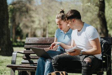 Fototapeta premium Two college students working on homework and discussing solutions while sitting on a bench in a sunny park.
