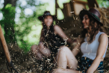 Two young women laughing and playing with hay inside a barn, having fun on a sunny day, representing joy, friendship, and rural lifestyle. © qunica.com