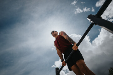 Focused male athlete training outdoors using workout equipment in a sunny urban park, displaying...
