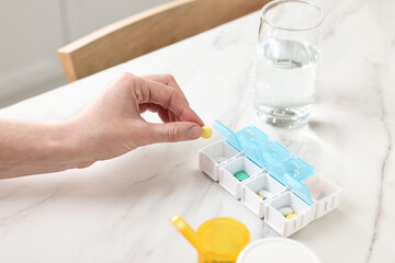 Woman with pills, organizer and glass of water at white marble table, closeup