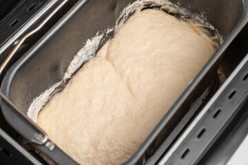 Breadmaker with raw dough on table, closeup