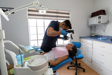 A dentist is examining a patient's teeth in a bright, modern dental clinic. The patient is seated in a dental chair, while the dentist, wearing gloves and a mask, uses dental tools for the check-up.