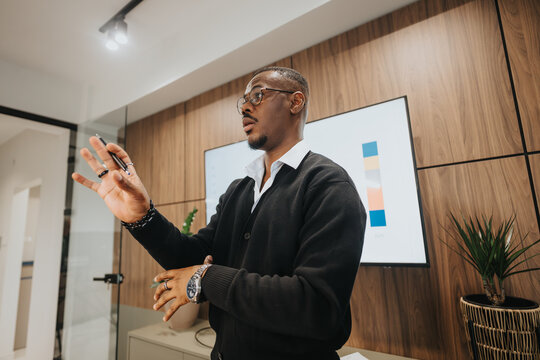 A young, mixed race entrepreneur presents growth statistics to colleagues in a well-lit, stylish meeting room, emphasizing teamwork and success.