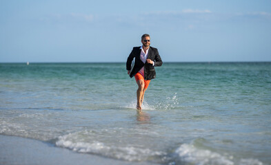 business success of businessman. Businessman in suit with laptop running in sea. successful businessman in wet suit at beach. businessman running at summer vacation. Beachside activities
