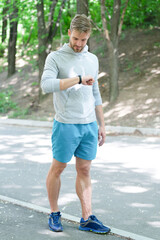 Man runner with fitness gadget. Smartwatch for fitness. Sporty fit man with sport equipment check time on smartwatch. Man tracking fitness results in sportswear outdoor. Use mobile application