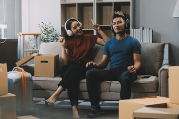 Asian sweet couple boyfriend, girlfriend sitting on sofa in cozy living room at home in morning, wearing headphones to listen music together with relaxation and happiness. Lifestyle, Love Concept