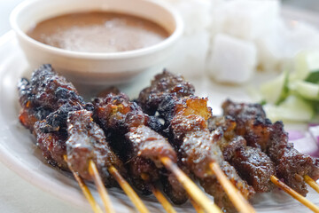 Close up view of satay (sate), a popular Malaysian street food.  Served together with peanut sauce, sliced cucumber, onion and rice cube (nasi impit)