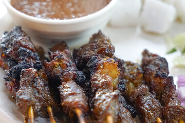 Close up view of satay (sate), a popular Malaysian street food.  Served together with peanut sauce, sliced cucumber, onion and rice cube (nasi impit)