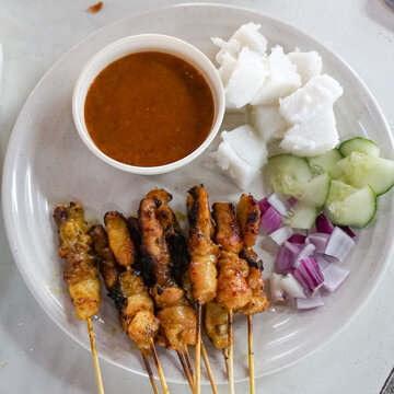 Top view of satay (sate), a popular Malaysian street food.  Served together with peanut sauce, sliced cucumber, onion and rice cube (nasi impit).