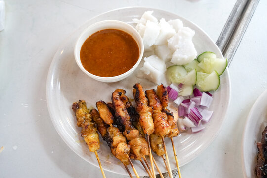Top view of satay (sate), a popular Malaysian street food.  Served together with peanut sauce, sliced cucumber, onion and rice cube (nasi impit).