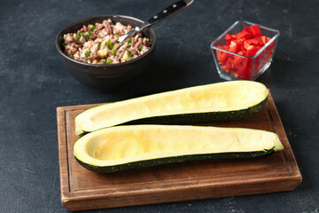 Wooden board with raw zucchini boats and ingredients on black background