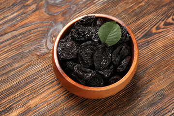 Bowl with tasty dried plums on wooden background