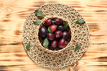 Wicker bowl with fresh ripe plums and leaves on wooden background