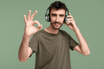 Handsome man in headphones showing OK on green background