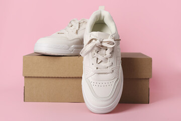 Cardboard box with stylish white sneakers on pink background
