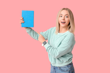 Beautiful young woman pointing at book on pink background