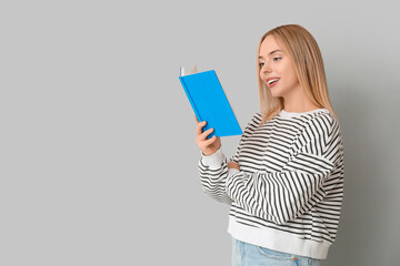 Beautiful young happy woman reading book on grey background