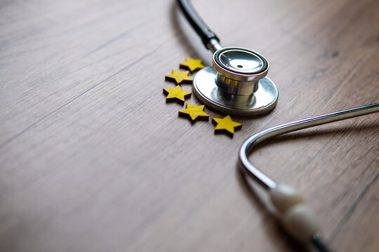 Closeup image of stethoscope and five stars on wooden table with copy space. Patient experience, satisfaction, review and rating concept.